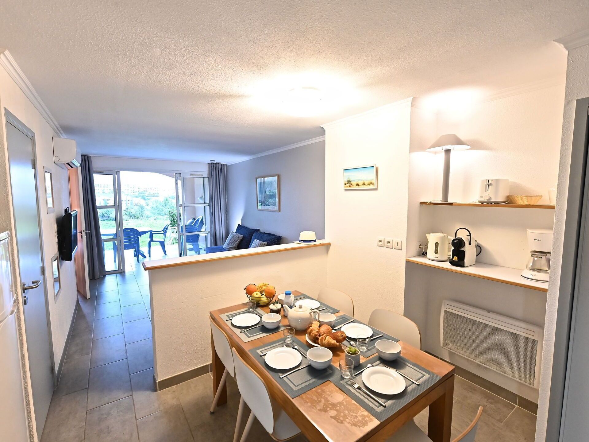 A dining area with a table set for four, a kitchenette with appliances, and a view of the outdoors.
