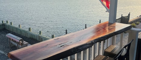 A wooden bar with two chairs, overlooking a body of water with a distant shoreline.