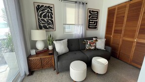 A living room with a grey sofa, two white ottomans, a side table with a lamp and a plant, and a wooden wardrobe. - Sunset Cove: Bayview, fantastic location, close to everything (Long Beach)