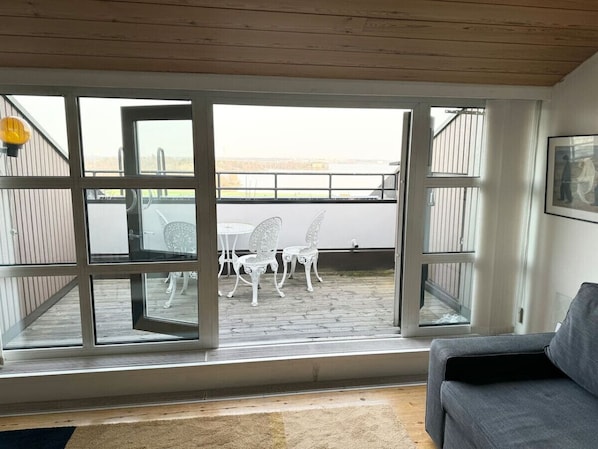 A room with a sliding glass door leading to an outdoor patio with white chairs and a table.