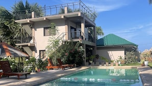 A multi-story building with a swimming pool, outdoor seating, and lush landscaping. - antipolo beach resort in tuburan (Tuburan)