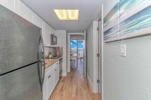 A narrow hallway with a kitchen on one side, a dining area with a view, and a door leading to an outdoor balcony.