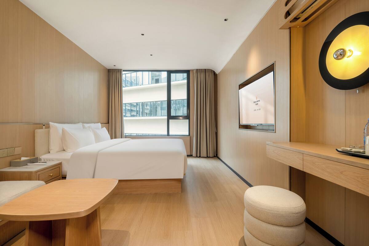 A modern hotel room with a large bed, a desk, a chair, and a view of the building outside.