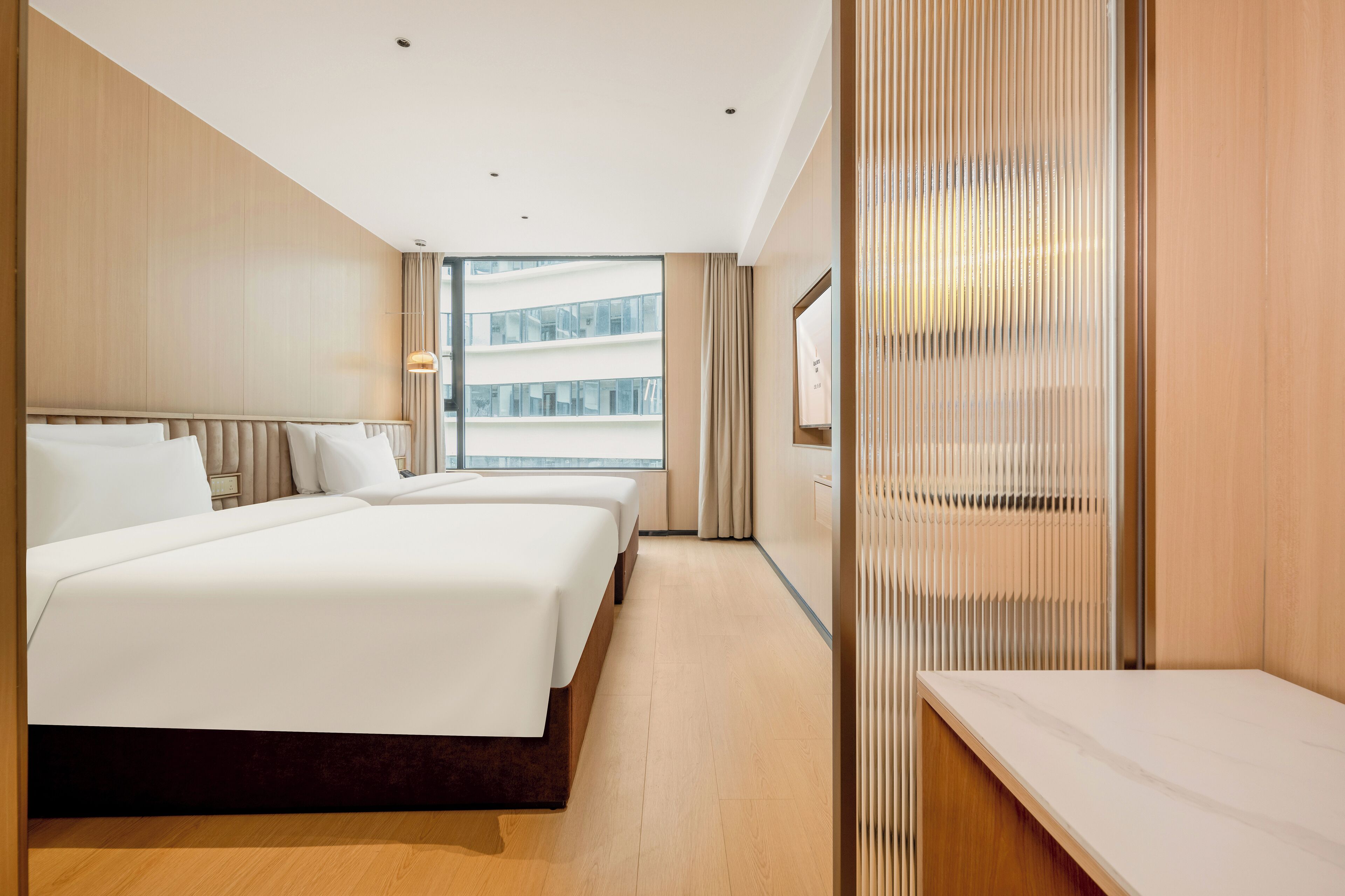 A modern hotel room with two beds, a large window, and a view of a building.