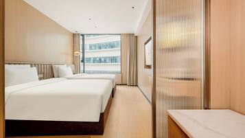 A modern hotel room with two beds, a large window, and a view of a building.