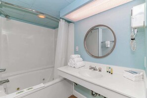 A bathroom with a bathtub, a sink with toiletries, a mirror, and a towel rack.