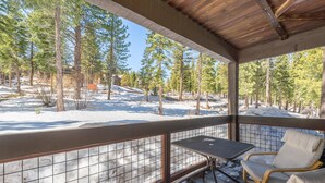Uma área externa coberta com mesa e cadeiras, com vista para uma paisagem nevada com árvores.