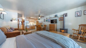 Um quarto aconchegante com uma cama grande, uma cadeira de balanço de madeira, uma mesa de jantar com cadeiras, uma área de cozinha e uma lareira.