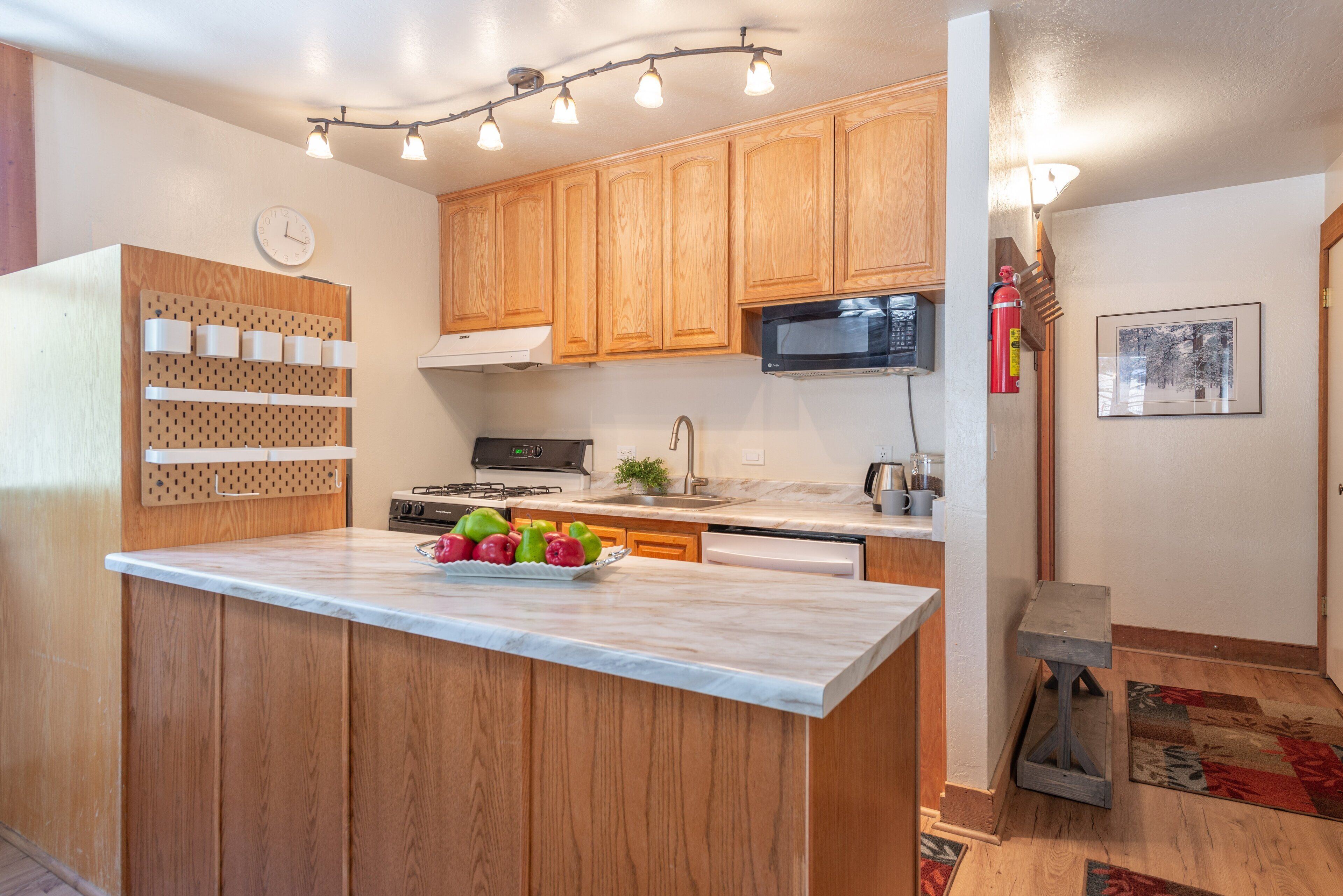 A kitchen with wooden cabinets, a marble countertop, a stove, a microwave, and a fruit bowl.