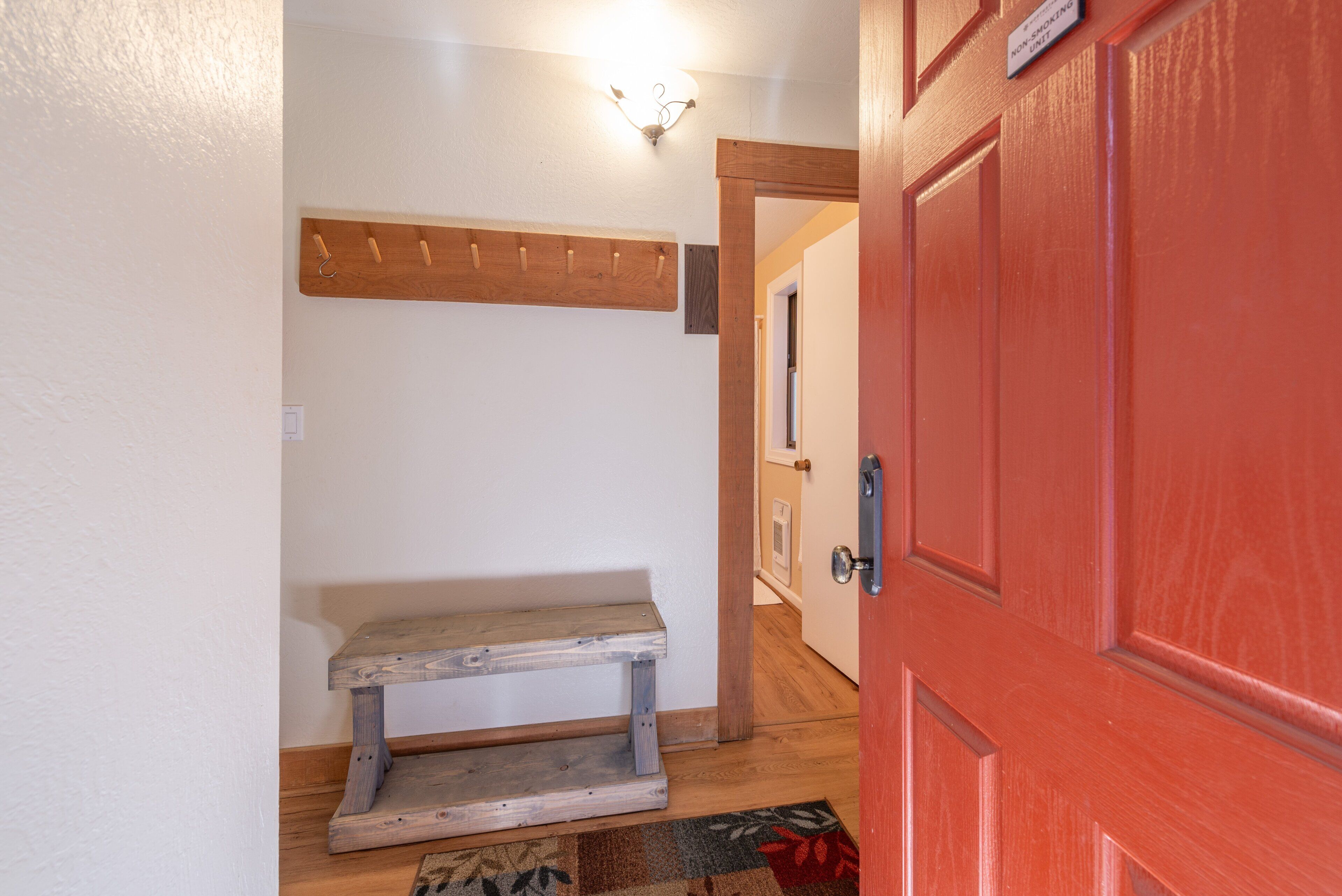 A wooden bench, a coat rack, and a red door in a hallway.