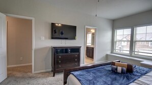 A bedroom with a bed, a dresser, a television, and a window with blinds. - Roseberg/Suglarland  3-BR - Extended Stay 30 days  (Rosenberg)