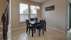 A dining area with a dark wooden table and chairs, a chandelier, and a window with blinds. - Roseberg/Suglarland  3-BR - Extended Stay 30 days  (Rosenberg)