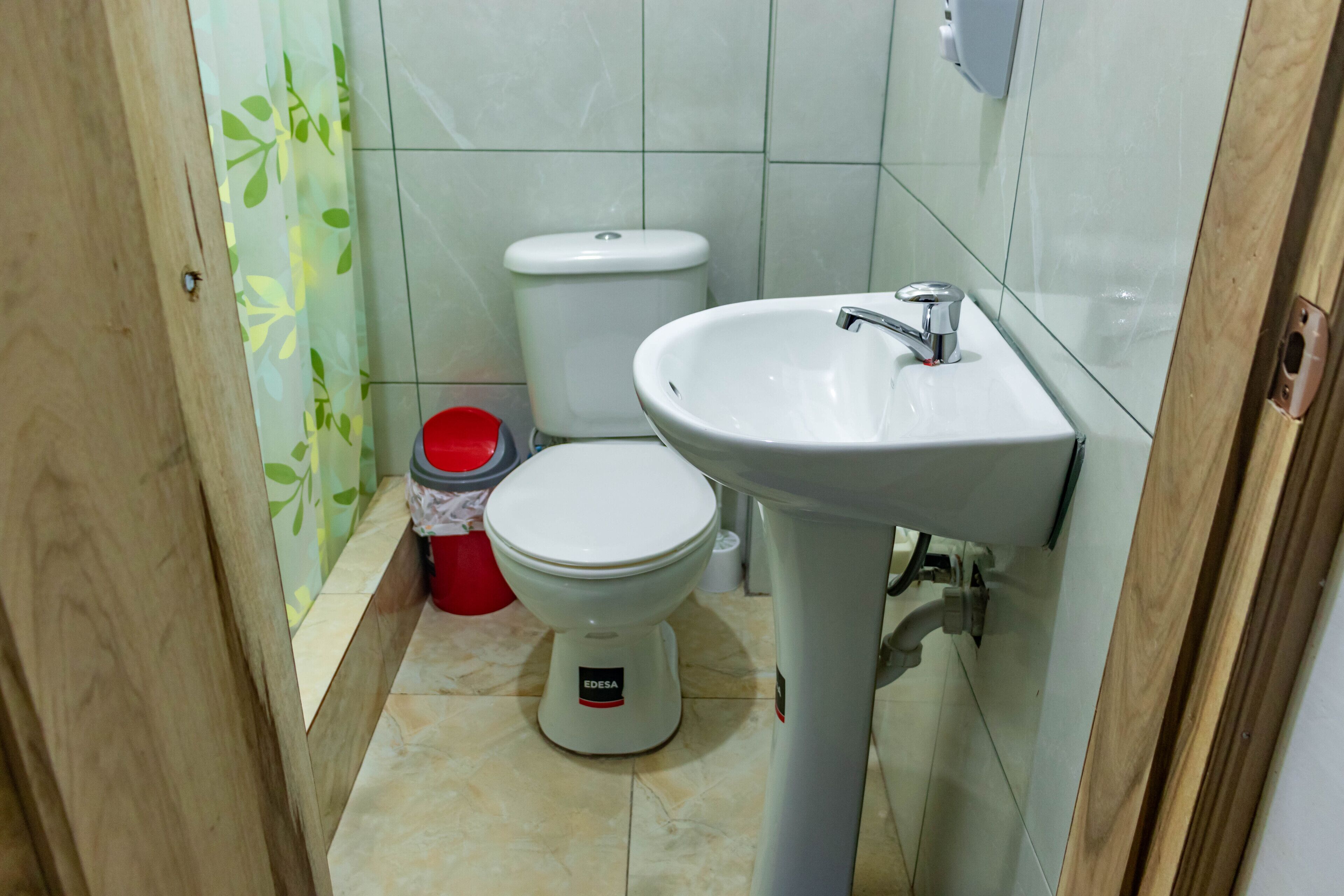 Un baño pequeño con un inodoro blanco, un lavamanos blanco y un balde rojo.