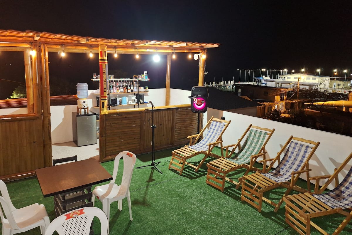 Un bar en la azotea con mobiliario de madera, dispensador de agua y una barra con diferentes botellas.