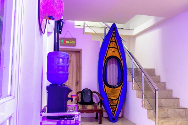 A hallway with a kayak leaning against the wall, a chair, a backpack, and a sign that reads "BANOS".
