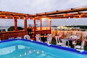 A pool area with a pergola, outdoor seating, and a view of the sea.