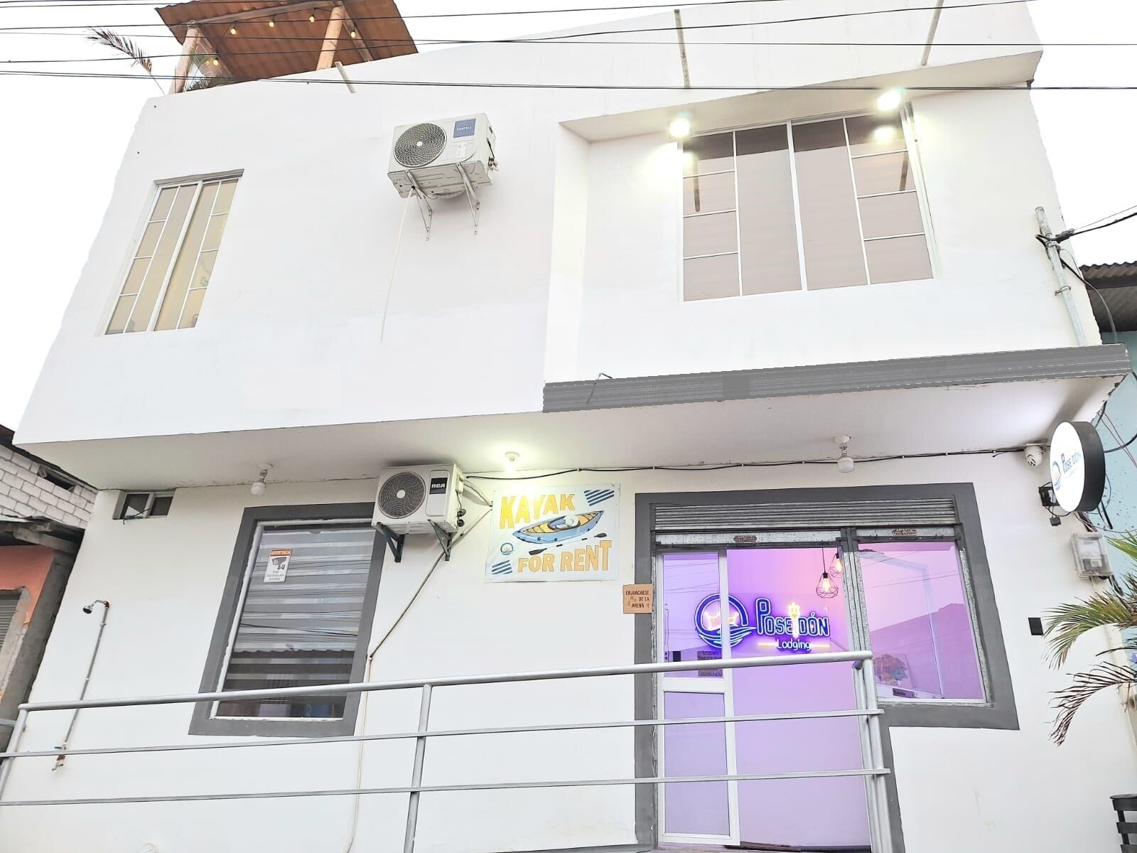 Un edificio de dos pisos con un letrero que dice 'Kayak for Rent' y 'Poseidon Lodging' en la planta baja.