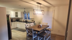 A modern kitchen with white cabinets, a wooden dining table with cushioned chairs, and a pendant light. - Balsam Retreat- Muskoka Getaway
Pet Friendly (Huntsville)