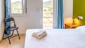 A hotel room with a bed, a chair, a nightstand with a lamp, and a view of the outdoors. - Sant Genis 19.2 Top floor apartment with terrace (Llança)