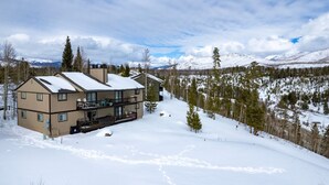 Un bâtiment à deux étages doté d’un balcon, entouré de montagnes et d’arbres couverts de neige.