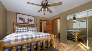 Une chambre avec un lit en bois, un ventilateur de plafond et un grand miroir qui reflète la pièce.