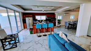 A spacious living area with a blue sofa, a kitchen with wooden cabinets, and a dining area with a table and chairs.