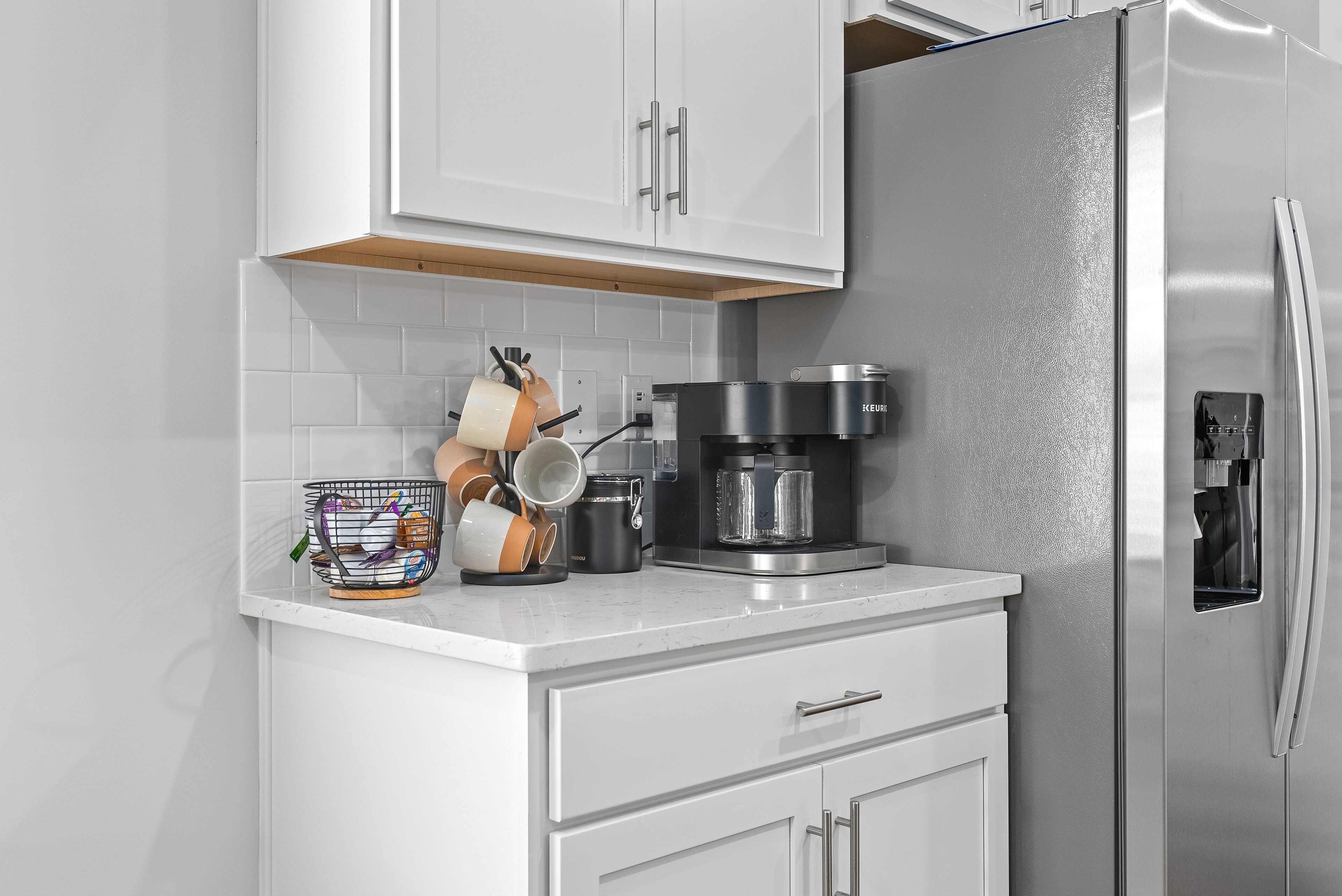 A modern kitchen with white cabinetry, a stainless steel refrigerator, and a coffee maker on the countertop.