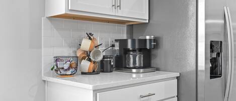 A modern kitchen with white cabinetry, a stainless steel refrigerator, and a coffee maker on the countertop.