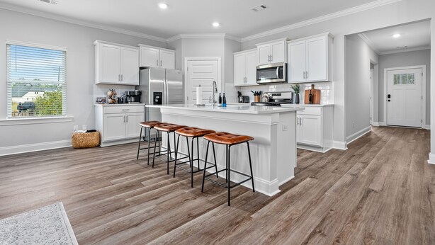 A modern kitchen with white cabinetry, a central island with stools, stainless steel appliances, and a view of the outdoors through a window.