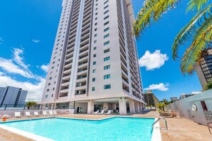 A high-rise hotel with a swimming pool, multiple balconies, and a clear blue sky.