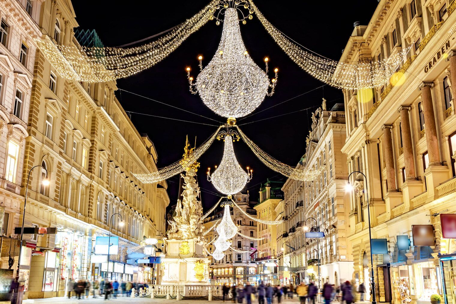 A historic street with ornate buildings, a central fountain, and festive decorations.