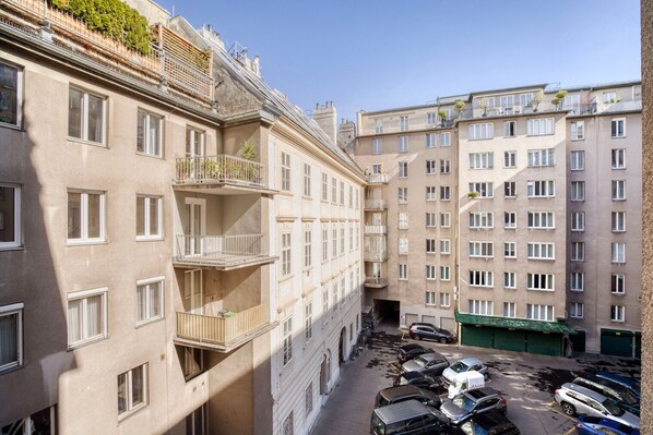 A multi-story residential building with balconies, a parking area with cars, and a narrow alleyway between the buildings.