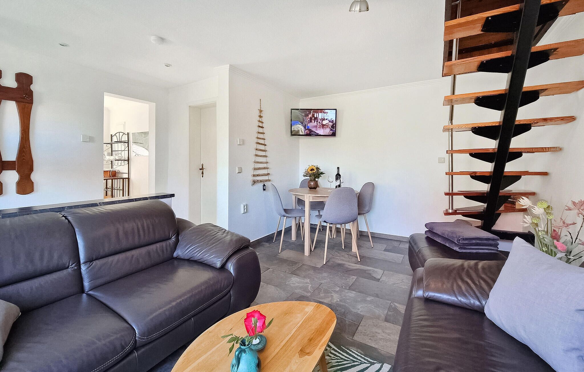 Una sala moderna con un sofá, una mesa de centro con un florero, una zona de comedor con sillas, un televisor y una escalera.
