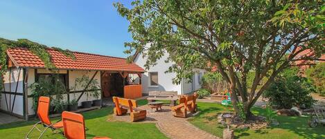 A garden with outdoor seating, a tree, and a building with a red-tiled roof.