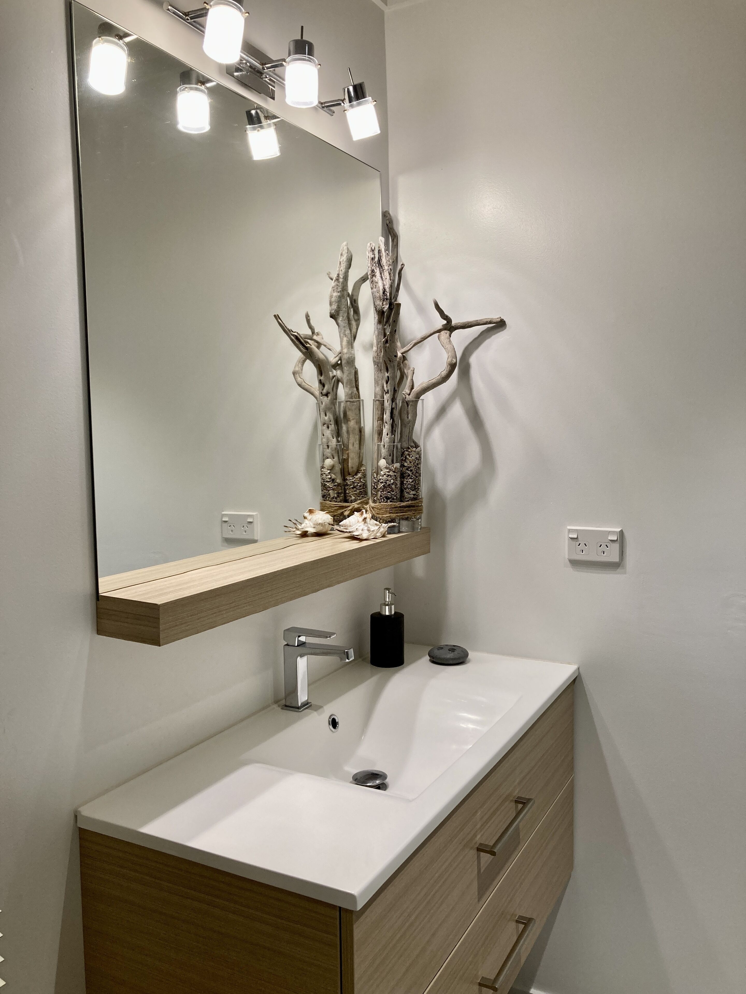A bathroom with a white sink, wooden vanity, and a mirror with lights.