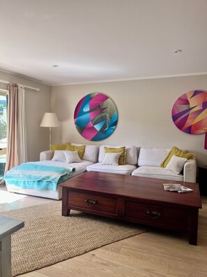 Een moderne hotelkamer met een bed, bank, bijzettafeltje en twee abstracte kunstwerken aan de muur.