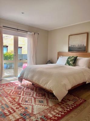 Ein Schlafzimmer mit einem Bett, einem gemusterten Teppich, einem Gemälde und Blick durch eine Glastür.