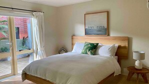 Un dormitorio amplio con una cama grande, cabecera de madera, un cuadro sobre la cama y vistas a un edificio de ladrillo rojo a través de un ventanal.