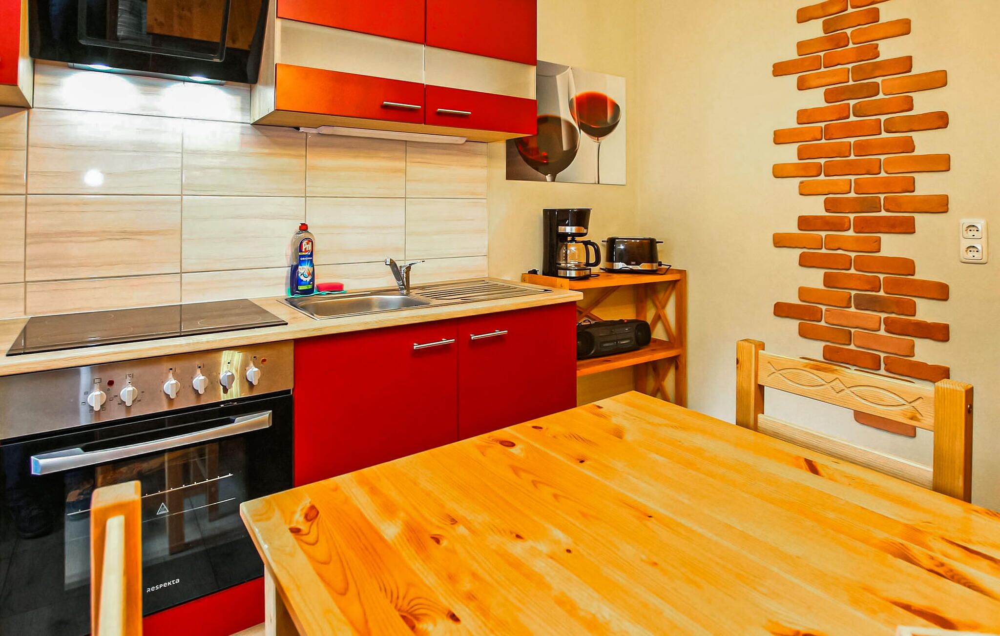Une cuisine de taille réduite avec des meubles de rangement rouges, une table en bois et un mur décoré d’un motif en briques.