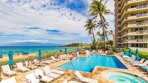A hotel pool area with lounge chairs, a hot tub, and palm trees. - Maui Resort Rentals: The Whaler 707 - Luxuriously Remodeled 7th Floor 1BR/2BA w/ Stunning Ocean and Mountain Views! (Lahaina)