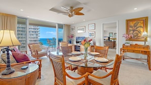 A spacious dining area with a glass table, wicker chairs, and a view of the ocean. - Maui Resort Rentals: The Whaler 707 - Luxuriously Remodeled 7th Floor 1BR/2BA w/ Stunning Ocean and Mountain Views! (Lahaina)