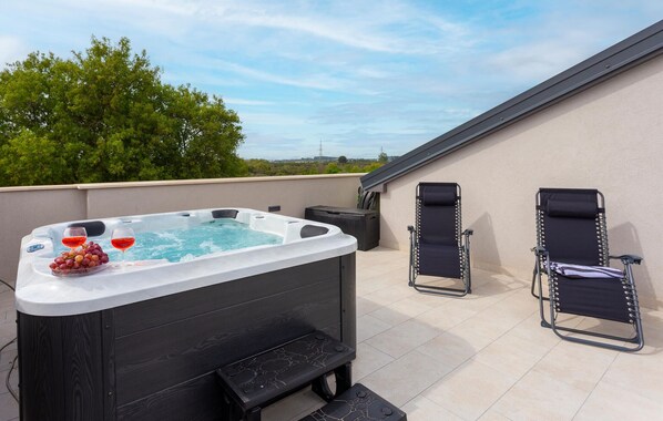 Terraço no telhado com banheira de hidromassagem, duas cadeiras de descanso e uma mesa com uvas e taças de vinho.