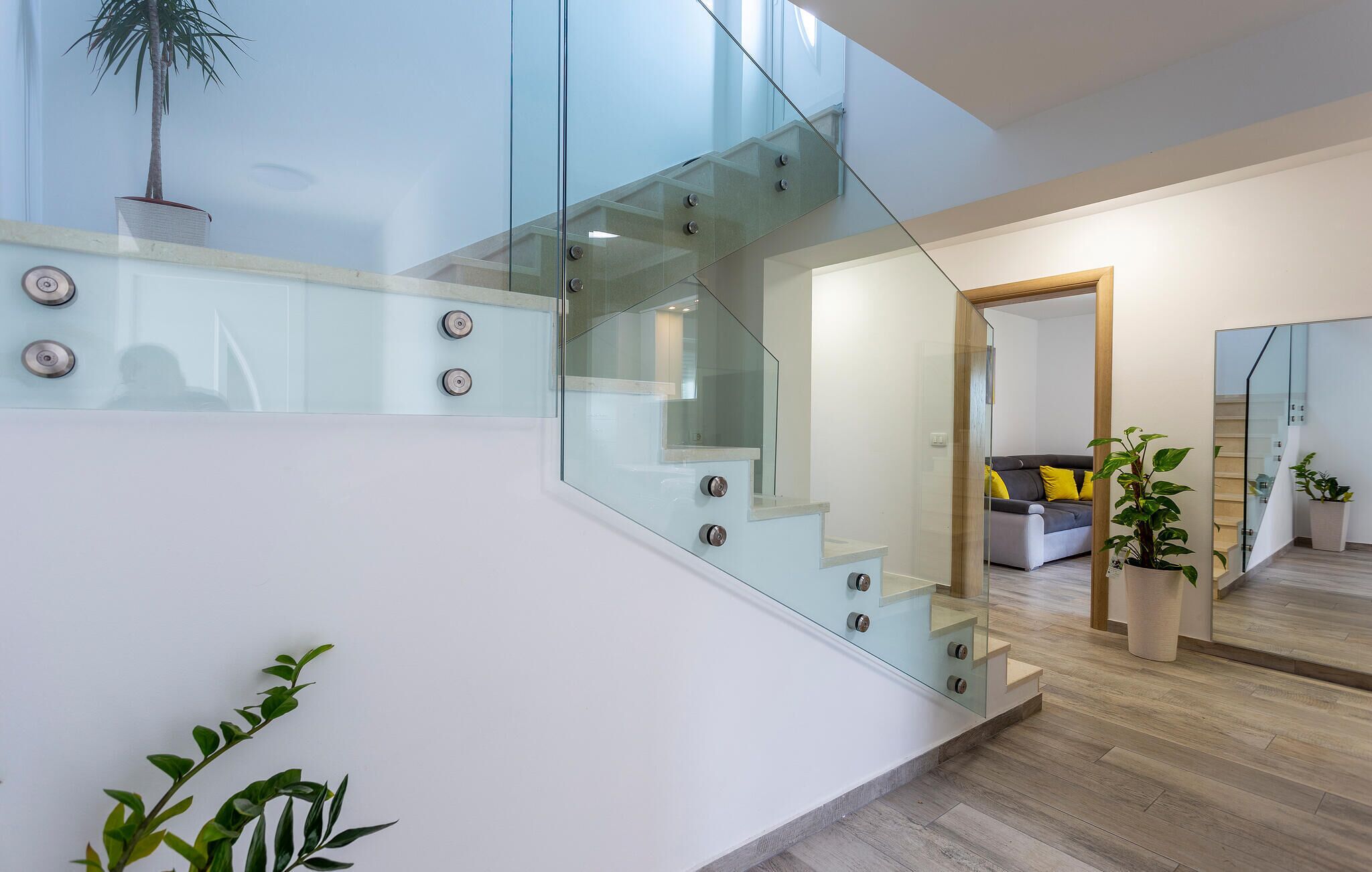 A modern interior with a glass staircase, a living area with a sofa, and potted plants.
