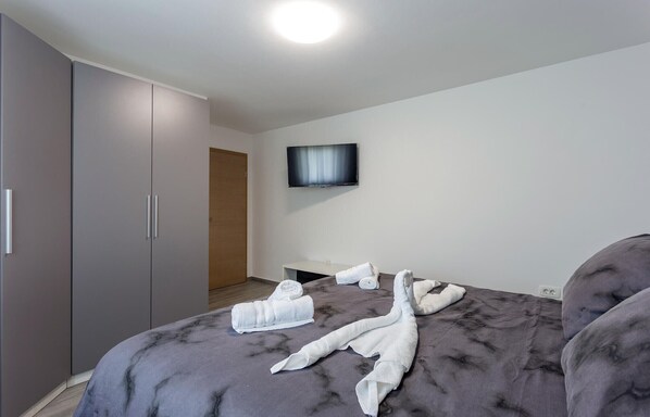 A modern hotel room with a large bed, grey upholstered headboard, a flat-screen TV mounted on the wall, and a wardrobe with sliding doors. - Nice home in Pula with WiFi (Pula)