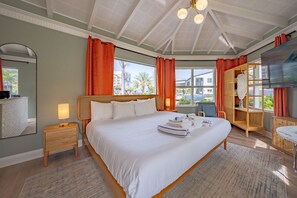 A spacious bedroom with a large bed, a wooden nightstand with a lamp, a wooden wardrobe, and a large window offering a view of the outside.