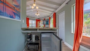 Cocina compacta con microondas, tostadora y cafetera sobre una estantería, refrigerador y ventilador de techo.
