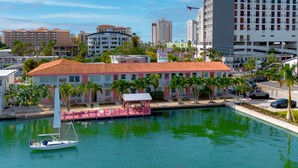 Una marina con un velero, un edificio de techo rojo y un hotel al fondo.
