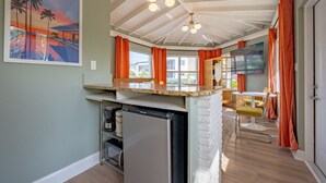 Una cocina con refrigerador empotrado, un comedor con una silla amarilla y un cuadro en la pared.