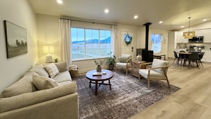 A modern living room with a sofa, armchairs, a coffee table, and a view of mountains through large windows.