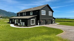A two-story black house with a large garage, surrounded by a well-maintained lawn and a gravel driveway.